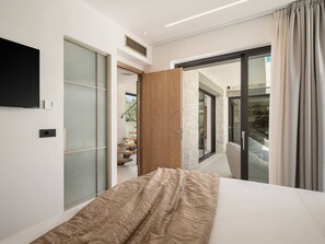 Un dormitorio moderno con una cama grande, un ventanal corredero que da a un balcón y un televisor montado en la pared.