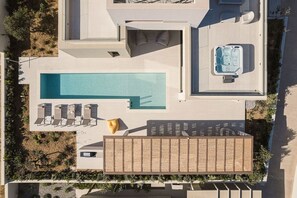 Luchtbeeld van een modern resort met een groot zwembad, ligbedden, een jacuzzi en een overdekte zitruimte buiten.