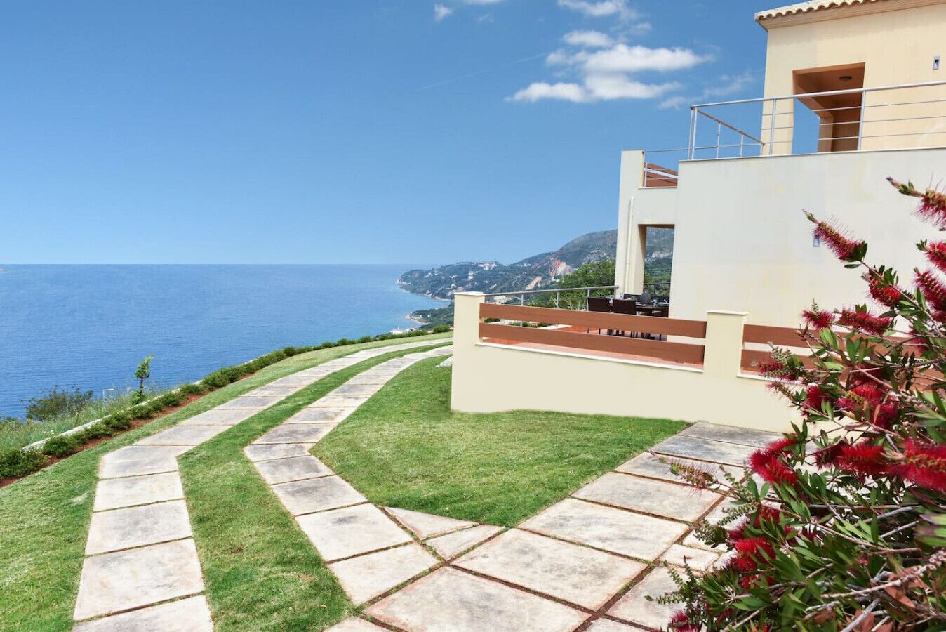 A modern building with a stone pathway leading to a grassy area overlooking the sea.