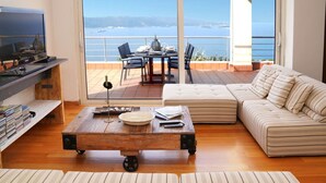 A living room with a sofa, a coffee table, a TV, and a balcony with a view of the sea. - Casa Minervos | Unique Views (Souda)