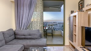 Un salon avec un canapé gris, un meuble pour la télévision et un balcon donnant sur des immeubles.