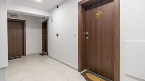 Un couloir avec deux portes en bois, un paillasson et un détecteur d’incendie.