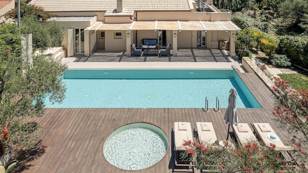 A swimming pool with a wooden deck, lounge chairs, and a small circular hot tub. - Villa Geraniotis | Chania (Gerani)