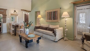 A cozy living room with a sofa, coffee table, and lamps. There is a dining area with chairs and a table. - Villa Geraniotis | Chania (Gerani)