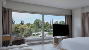 Une chambre d’hôtel moderne dotée d’une grande fenêtre, d’un téléviseur à écran plat, d’un canapé, d’une table ronde et d’un lit.