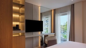 Une chambre d’hôtel moderne dotée d’un grand lit, d’un téléviseur fixé au mur, d’un coin salon avec un fauteuil et offrant une vue sur l’extérieur.