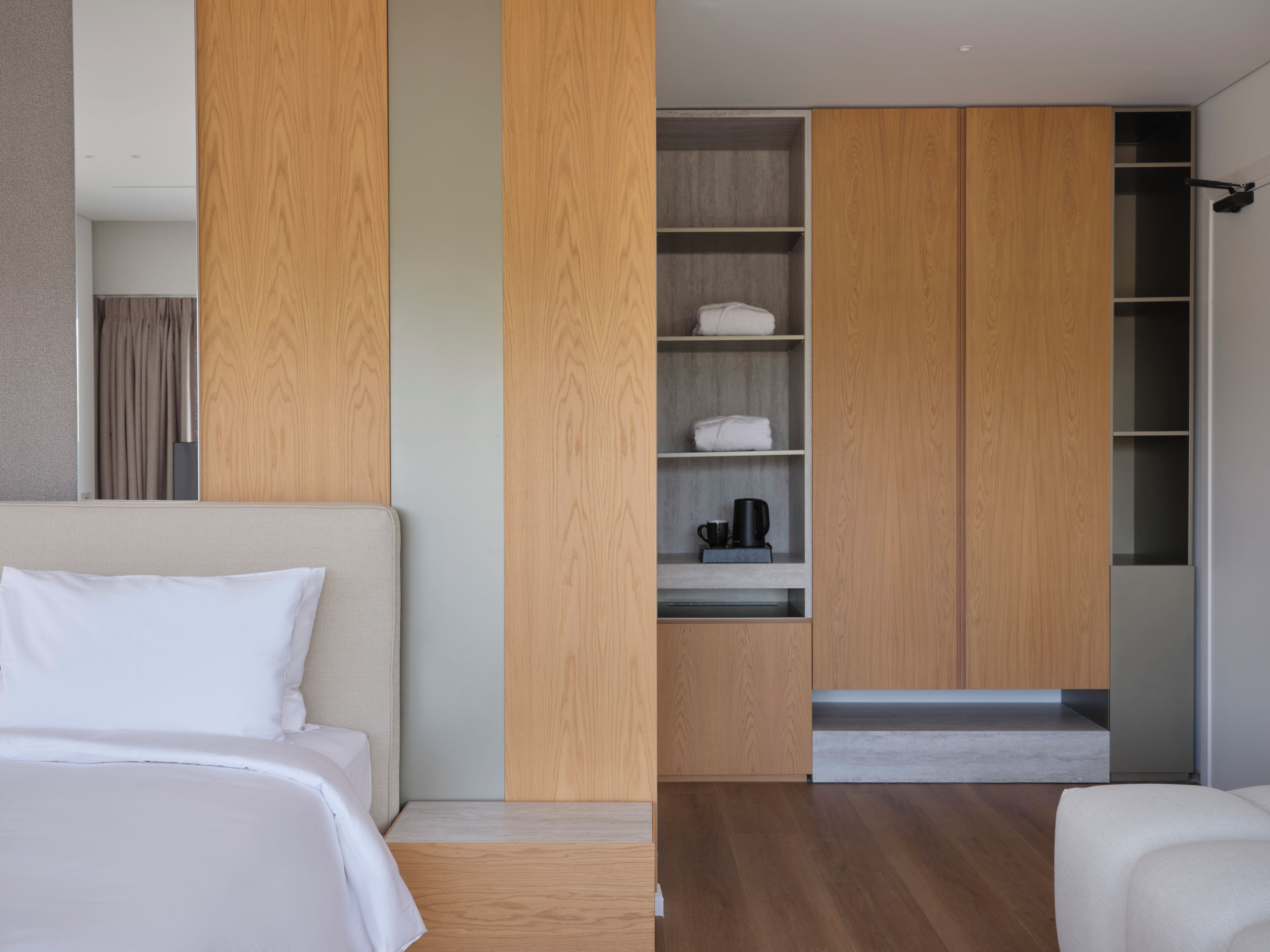 Una habitación de hotel moderna con una cama grande, un armario de madera y un estante empotrado con toallas y una cafetera.