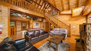 A wooden cabin interior with a pool table, leather sofas, a staircase, and a stone fireplace. - Smoky Mountain Cinema: Showtime in the Smokies (Sevierville)