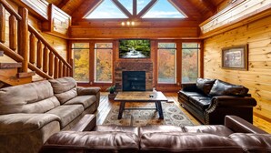 A log cabin interior with a fireplace, wooden walls, and a wooden staircase. - Smoky Mountain Cinema: Showtime in the Smokies (Sevierville)