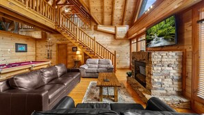 A cozy log cabin interior with a wooden staircase, leather sofas, a fireplace, and a billiards table. - Smoky Mountain Cinema: Showtime in the Smokies (Sevierville)