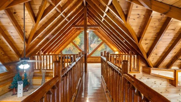A wooden attic room with a central wooden beam structure, a wooden floor, and a view of trees through a large window. - Smoky Mountain Cinema: Showtime in the Smokies (Sevierville)