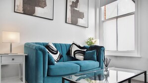 A modern living room with a teal sofa, a glass coffee table, a white side table, and abstract art on the wall. - WhiskAwayStays No. 58 Studio  No. 2 (Worcester)