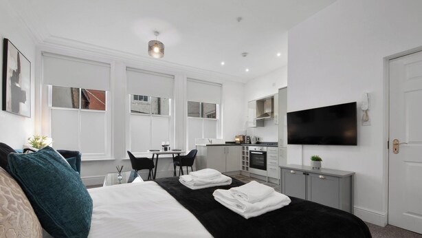 A modern hotel room with a large bed, a desk, a kitchenette, and a TV mounted on the wall. - WhiskAwayStays No. 58 Studio  No. 2 (Worcester)