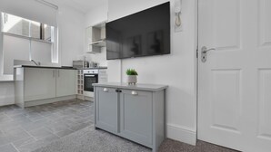 A modern kitchen with grey cabinets, a built-in oven, and a flat-screen TV mounted above the cabinets. - WhiskAwayStays No. 58 Studio  No. 2 (Worcester)