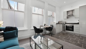 A modern kitchen with white cabinets, a built-in oven, and a dining area with a glass table and chairs. - WhiskAwayStays No. 58 Studio  No. 2 (Worcester)