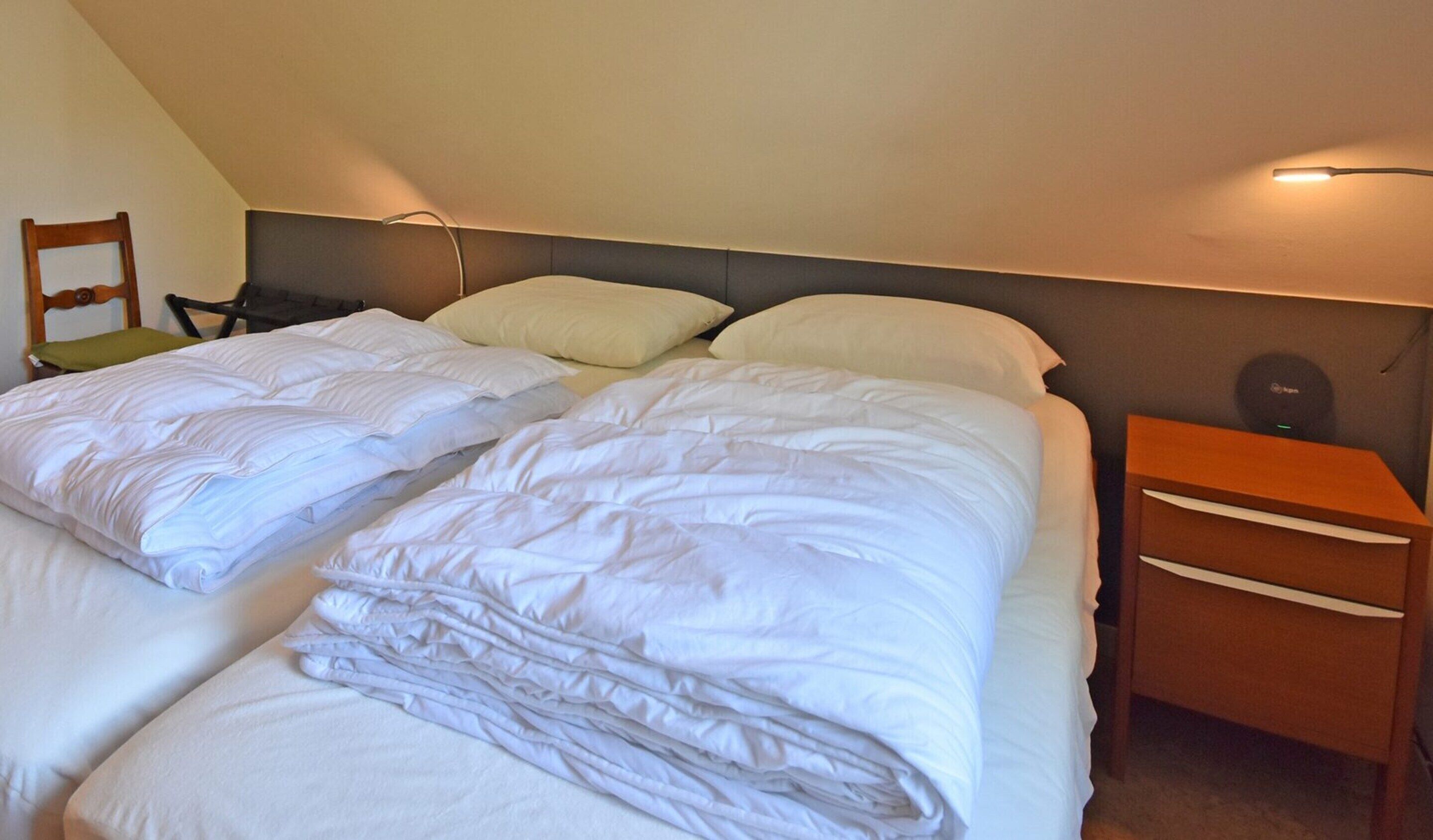 A twin room with two beds, a nightstand, a chair, and a wall-mounted lamp.