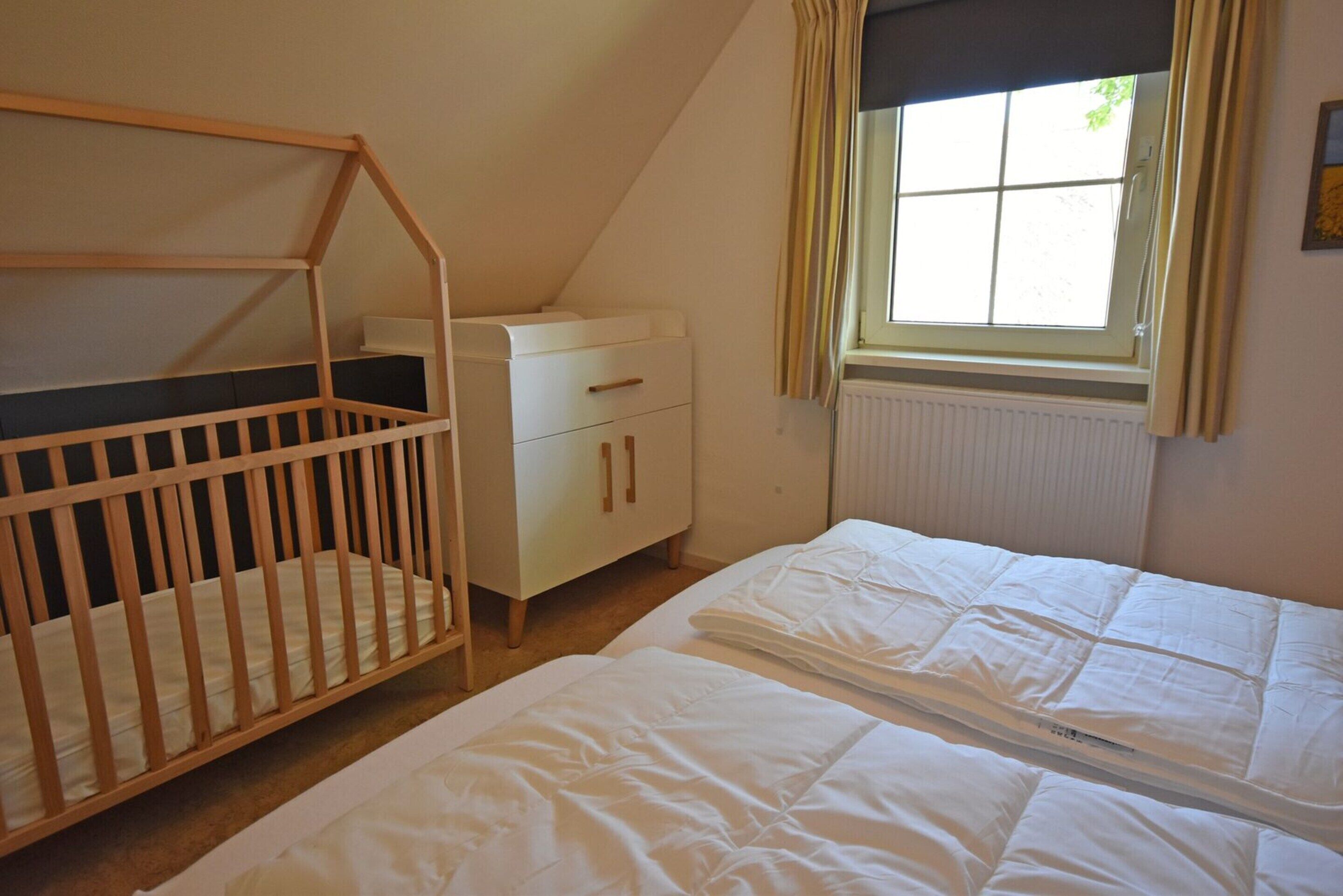 A bedroom with a crib, a dresser, and a window with curtains.