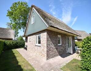 Et traditionelt hus med stråtækt tag, murstensvægge og en lille veranda med en bænk.