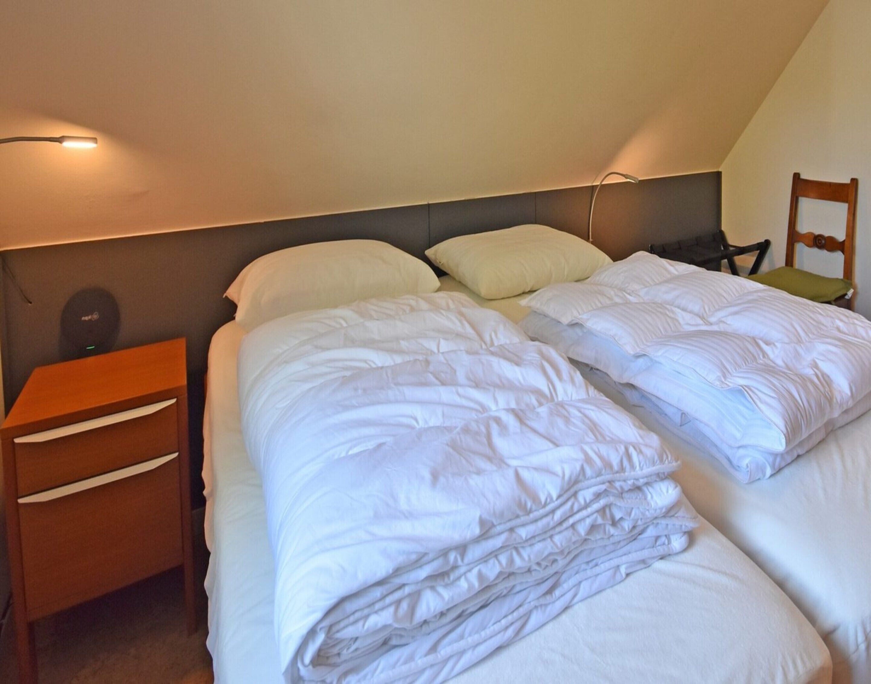 A bedroom with two beds, a nightstand, and a chair.