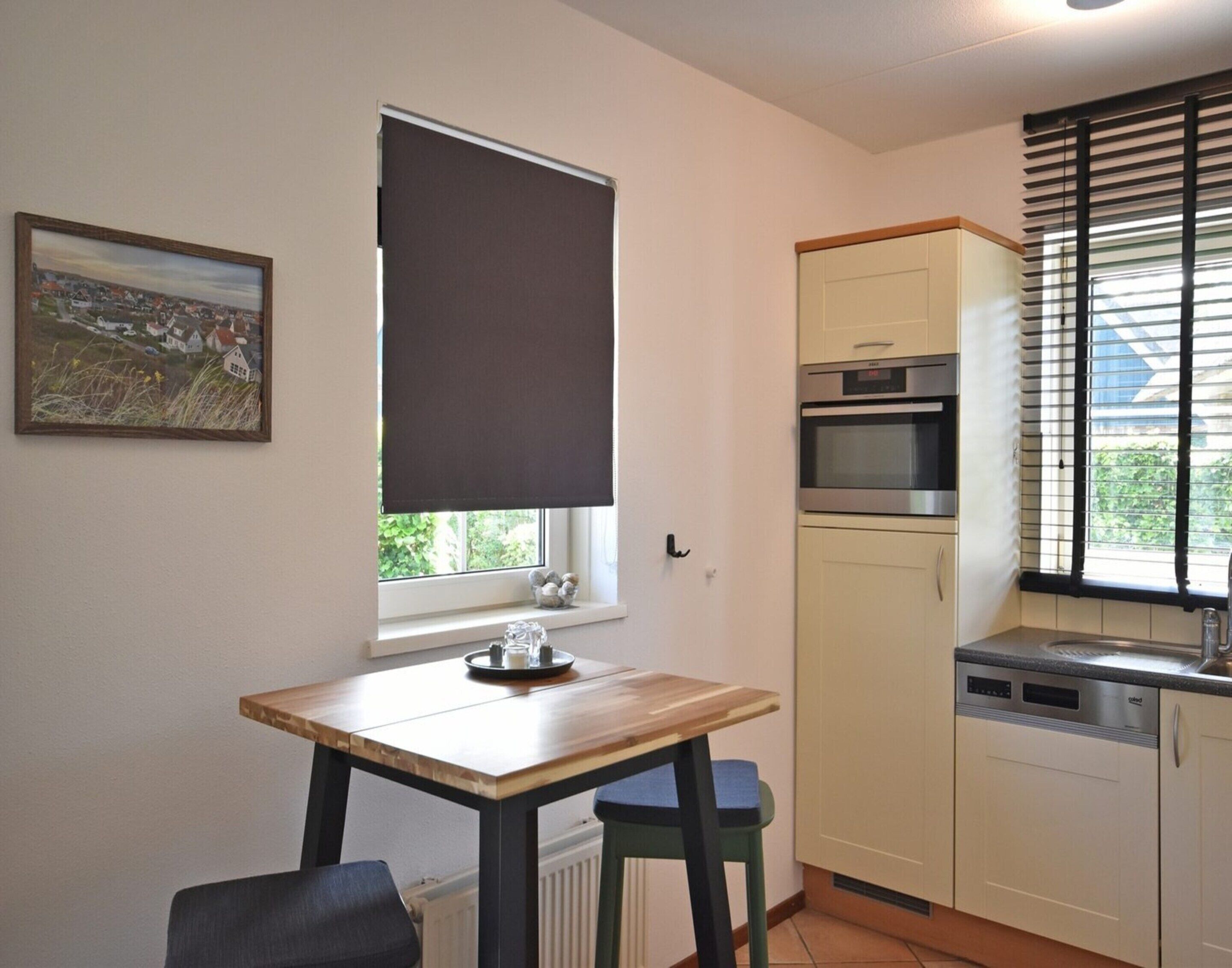 A compact kitchen with a dining table, a window with a blind, a built-in oven, and a sink.