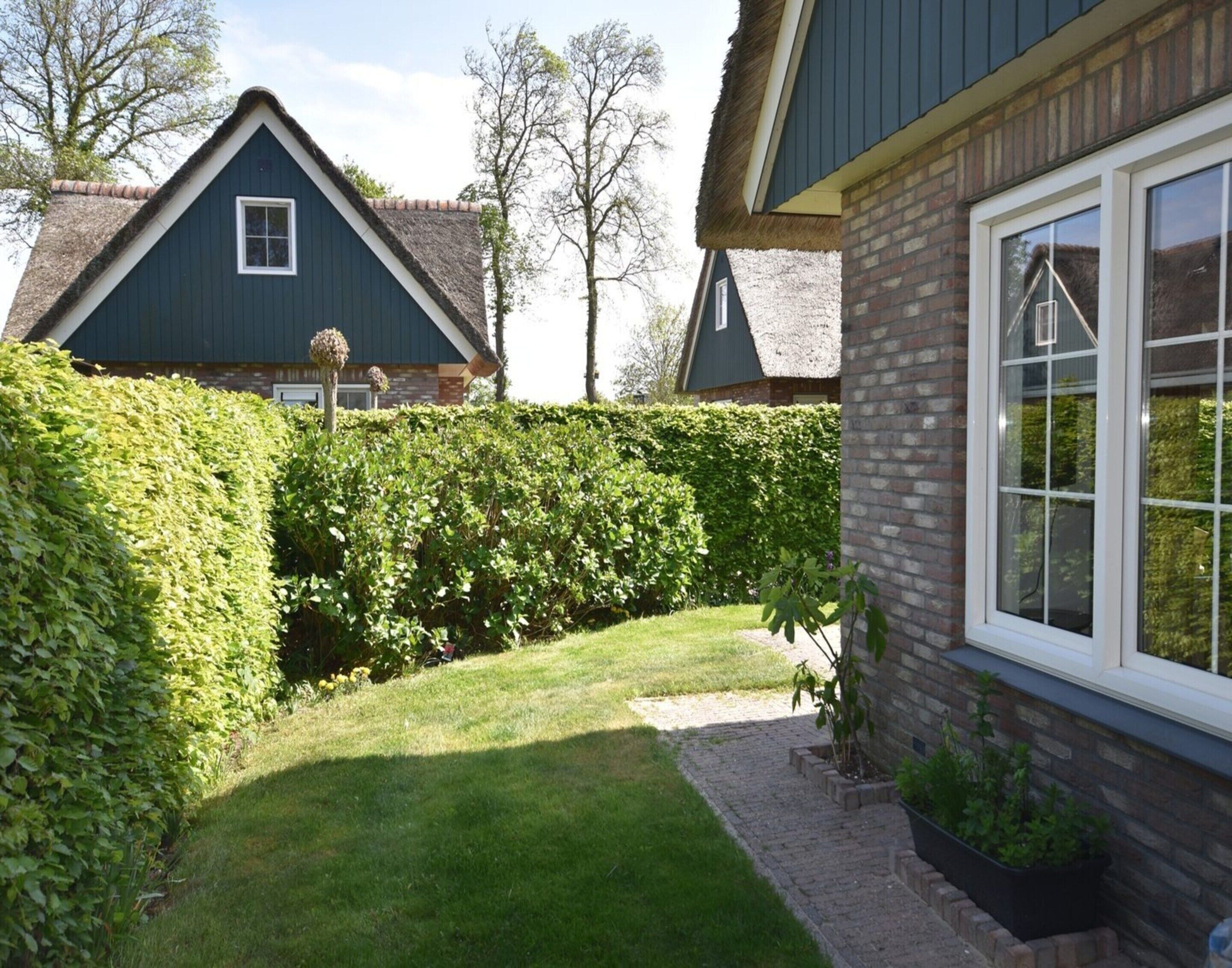 A residential property with a well-maintained garden, a brick exterior, and a thatched roof house in the background.