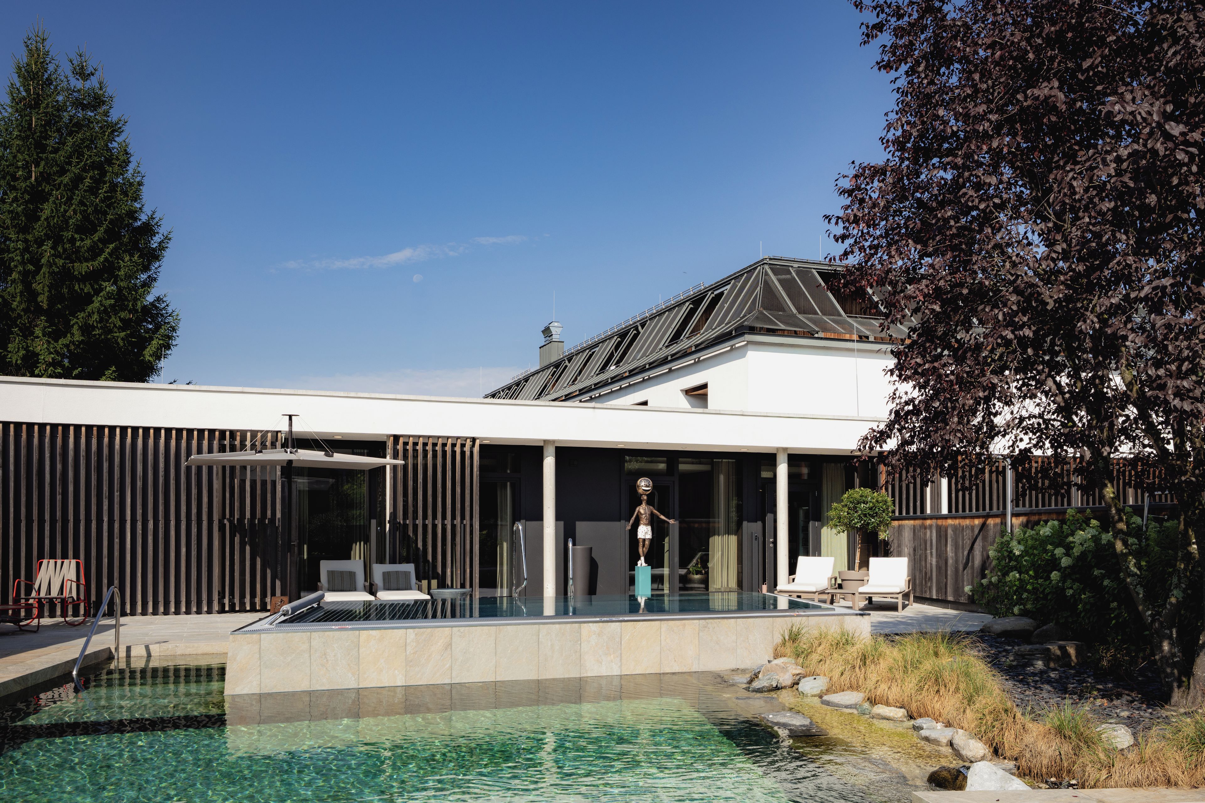 A modern house with a swimming pool, a covered patio, and a view of the sky.