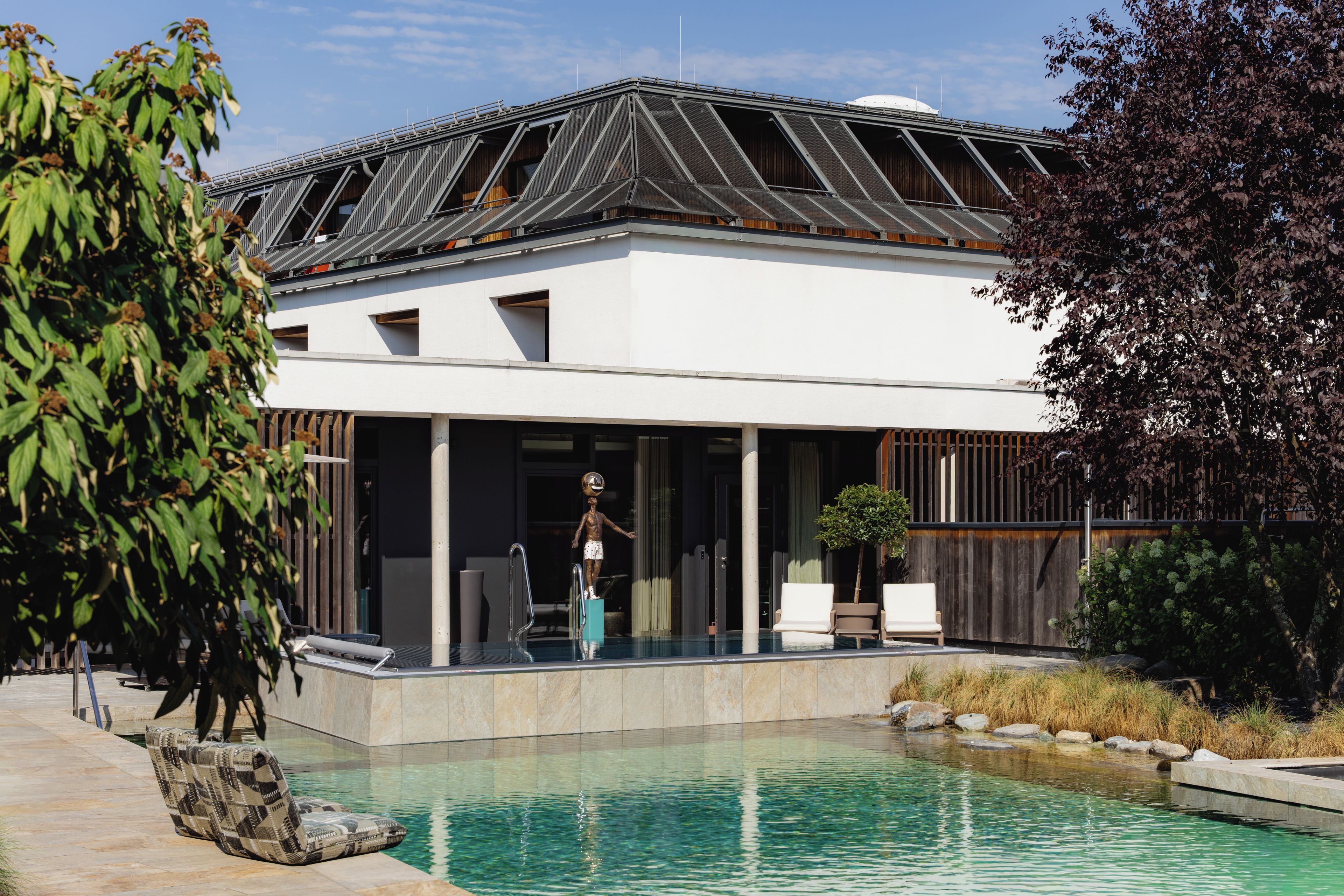 Una casa moderna con piscina, terraza techada y una estatua.