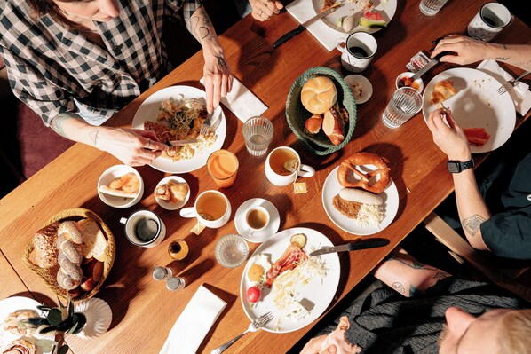 Un groupe de personnes est assis autour d’une table en bois, et on peut y voir différents plats, des boissons et du pain.