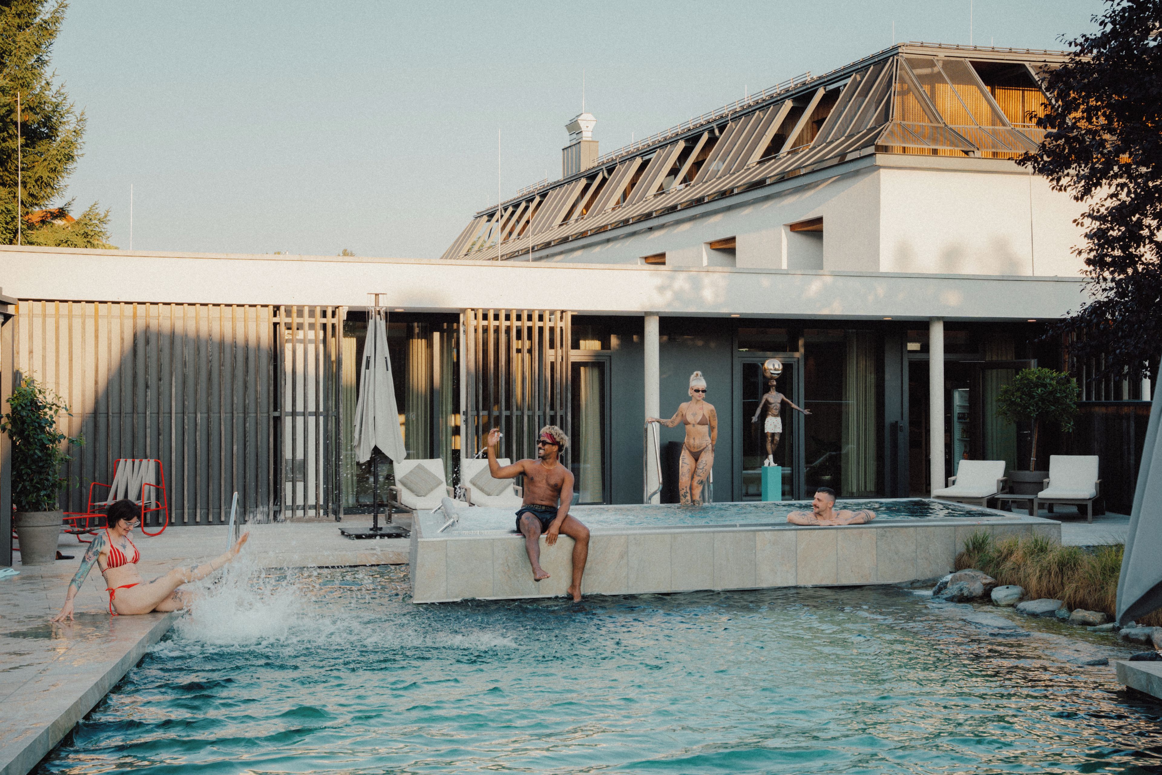 Un área de piscina moderna con vista despejada, sillas de descanso y un edificio con techo inclinado.