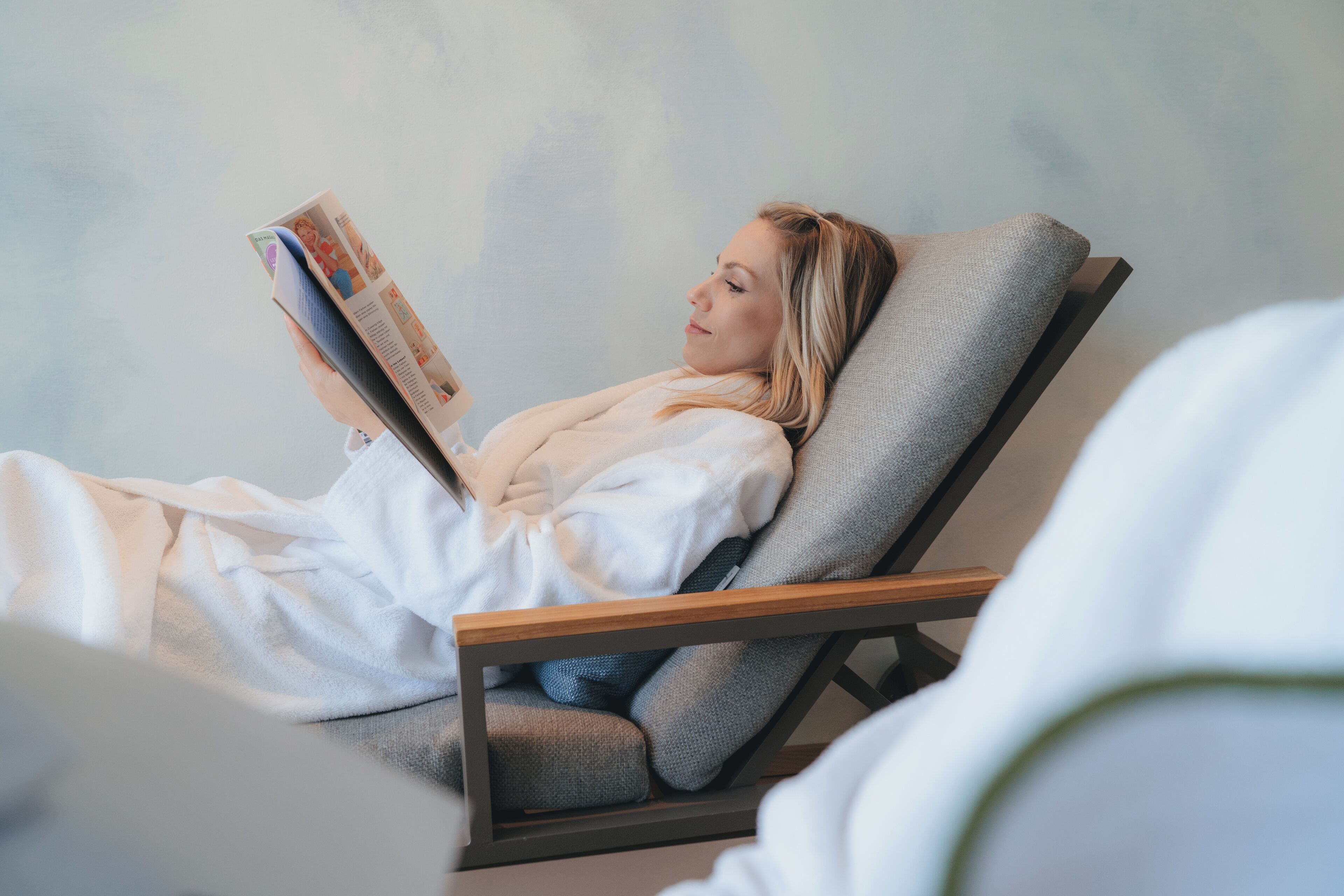 Una persona recostada en una silla reclinable leyendo una revista.
