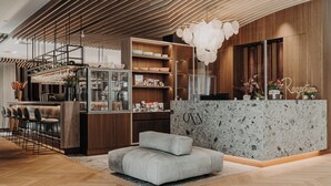 A modern reception area with a wooden reception desk, a seating area with a grey sofa, and a bar with glassware.