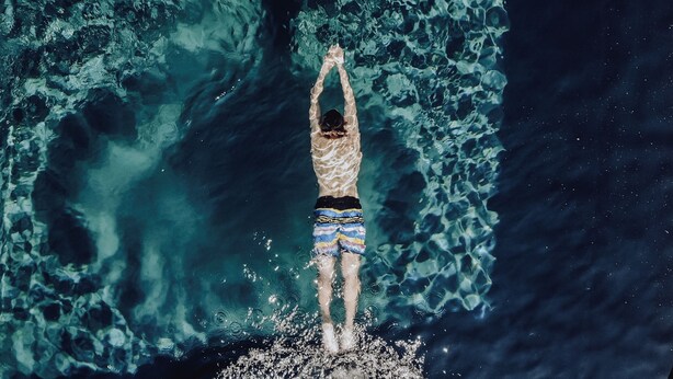 A person standing on a rock with arms raised, surrounded by clear blue water.