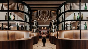 A bar area with curved wooden shelves displaying bottles, a central decorative vase, and a patterned ceiling.