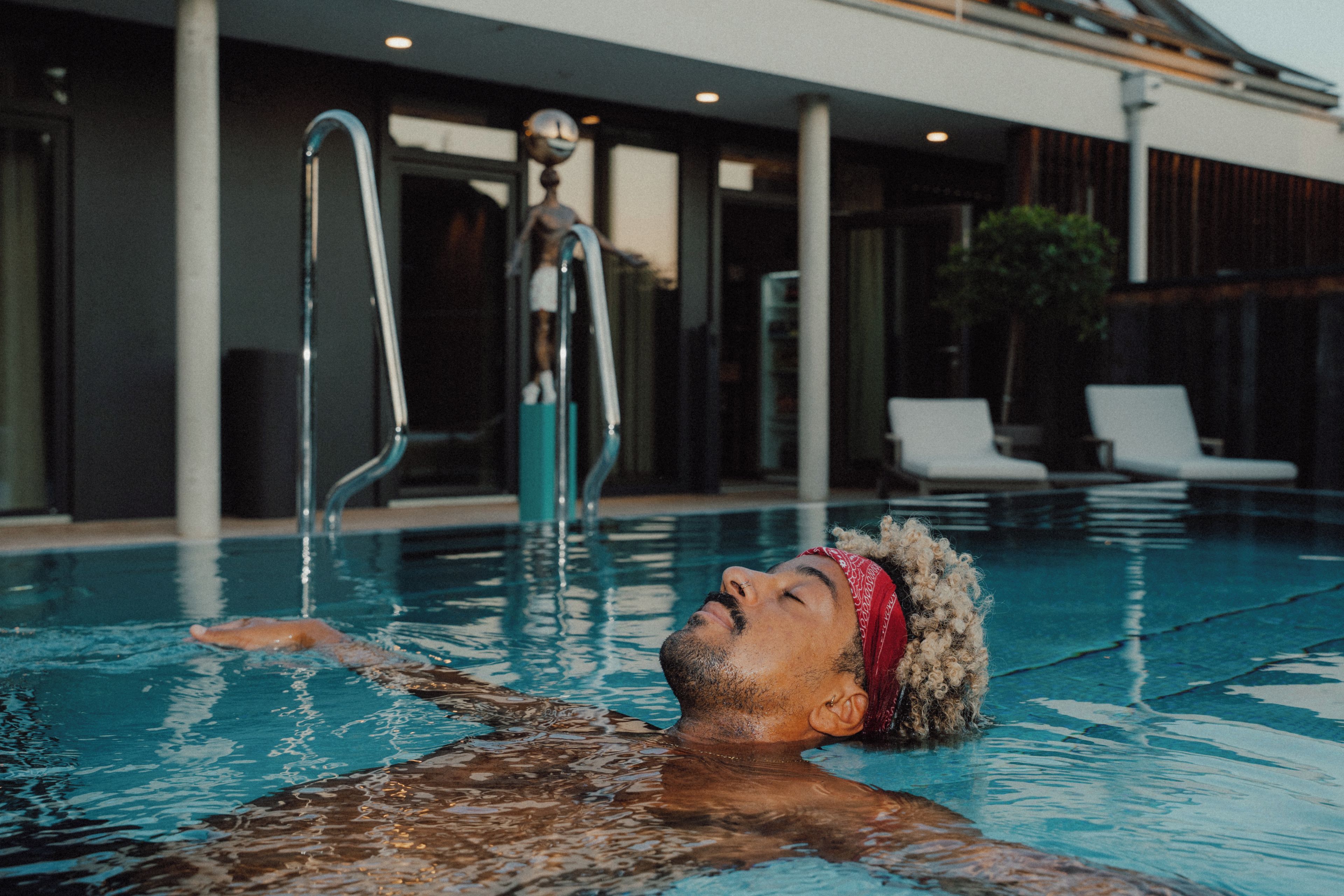 A person in a swimming pool with a clear view of a modern building in the background.