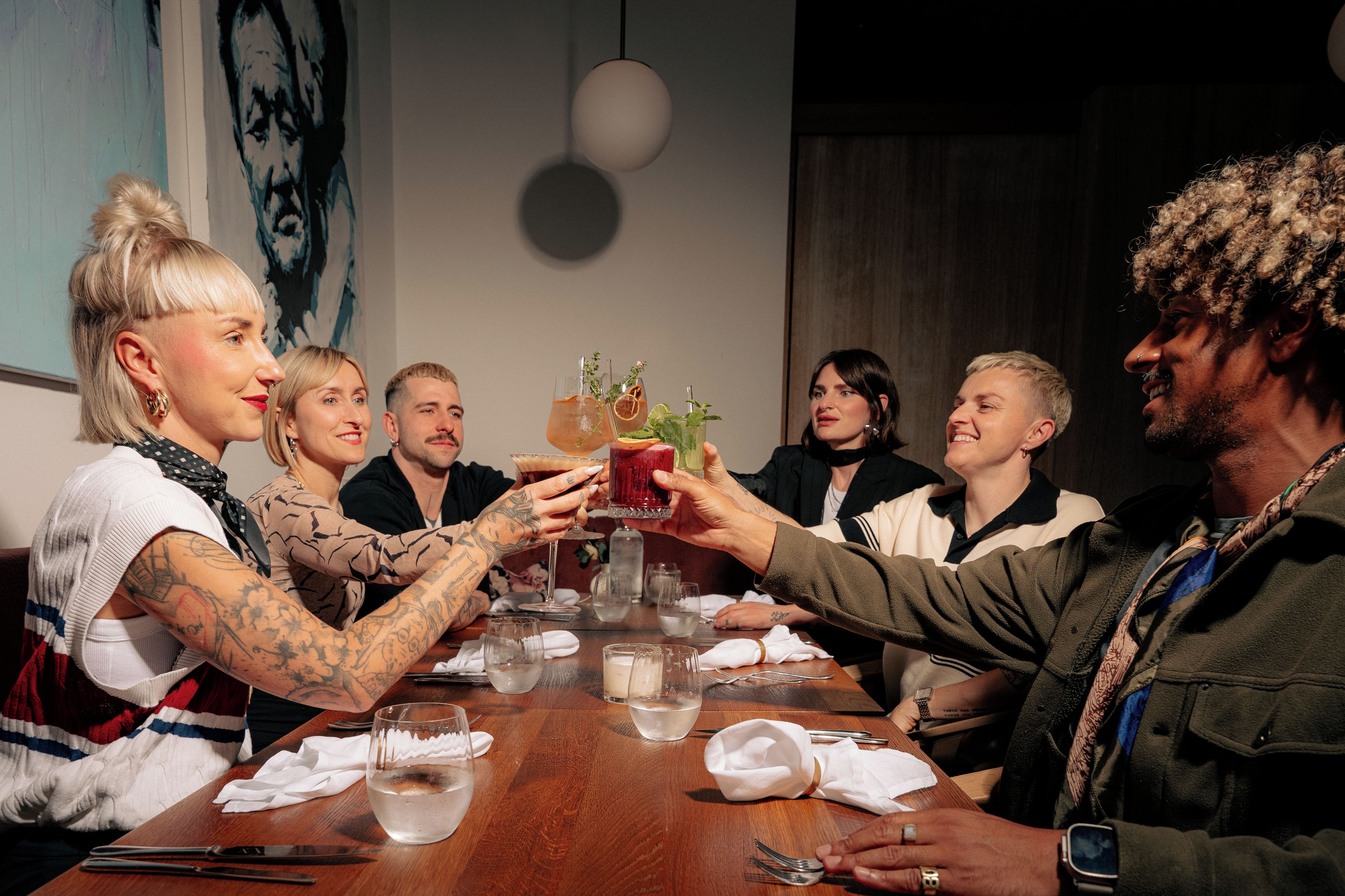 A group of people toasting at a wooden table with drinks and glasses.