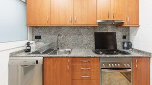 A compact kitchen with wooden cabinets, a granite countertop, a dishwasher, a stove, and a coffee maker. - Vistas SAGRADA FAMILIA piso grande y luminoso (Barcelona)