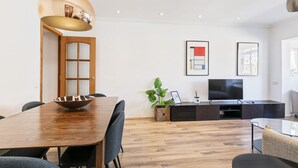 A modern living room with a wooden dining table, a TV, and a large window. - Vistas SAGRADA FAMILIA piso grande y luminoso (Barcelona)
