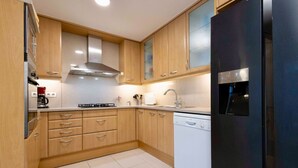 A modern kitchen with wooden cabinets, a stainless steel range hood, a dishwasher, and a black refrigerator. - Apartamento para 6 amplio y luminoso en Bonanova (Barcelona)