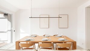 A dining area with a wooden table set for six, surrounded by six chairs, with a modern pendant light fixture above.