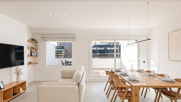 A modern living room with a sofa, TV, and dining area with a table set for six.