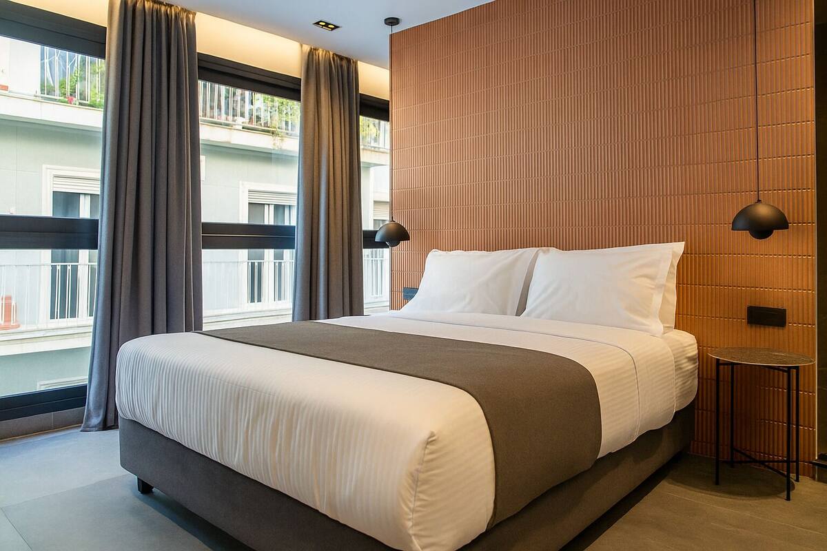 A modern hotel room with a large bed, a small bedside table, and a view of the outside balcony.