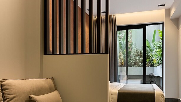 Una habitación de hotel moderna con sofá, cama y vistas a la vegetación a través de amplias ventanas.