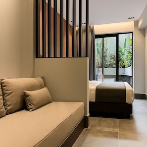 Ein modernes Hotelzimmer mit einer Couch, einem Bett und Blick auf Grün durch große Fenster.