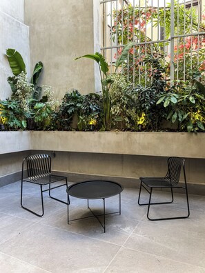 A courtyard with two black metal chairs and a small round table, surrounded by a variety of green plants and flowers. - NOOS Acropolis (Athens)