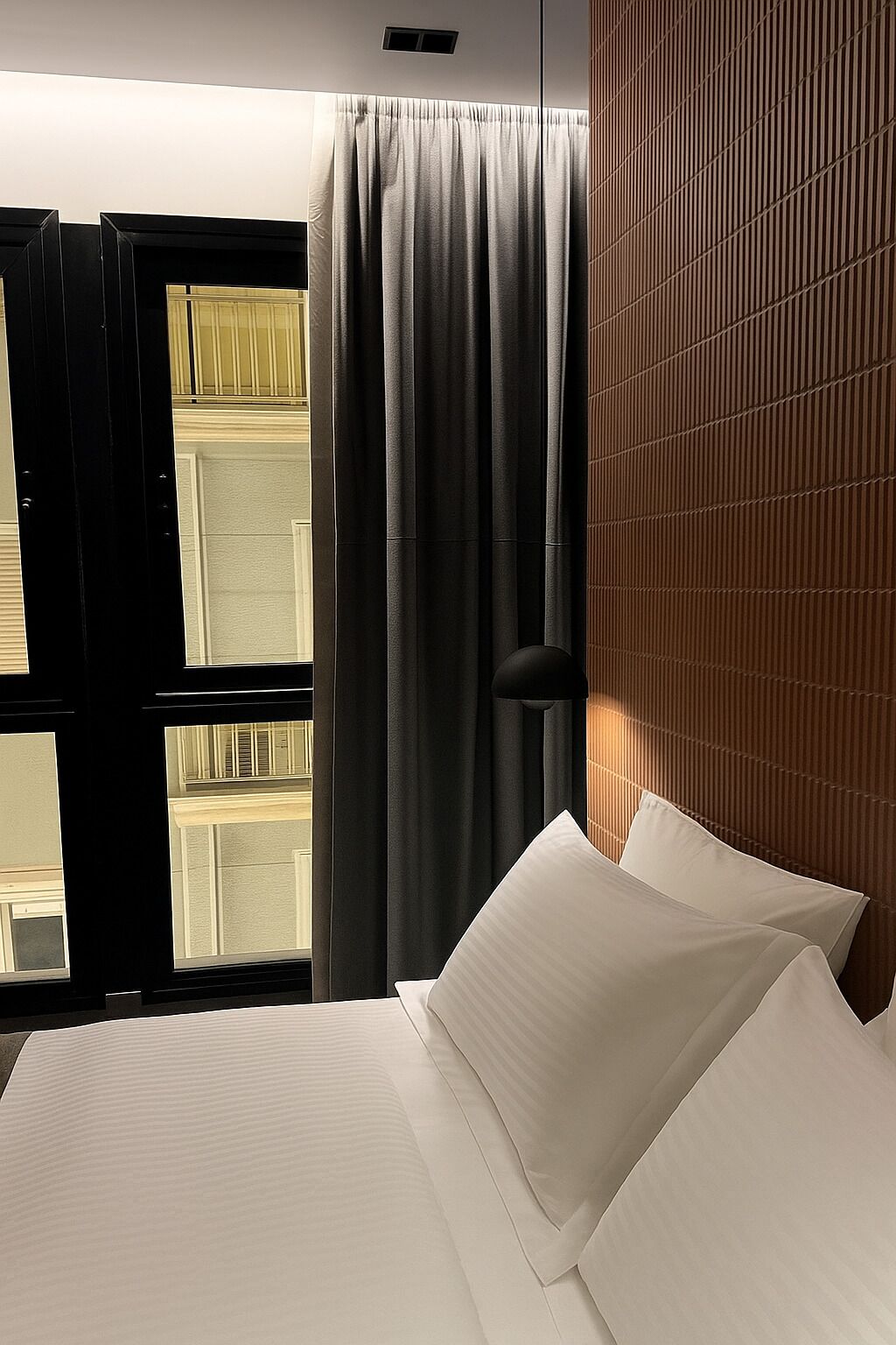 Ett hotellrum med en säng, ett fönster med gardiner och en sänggavel i trä.