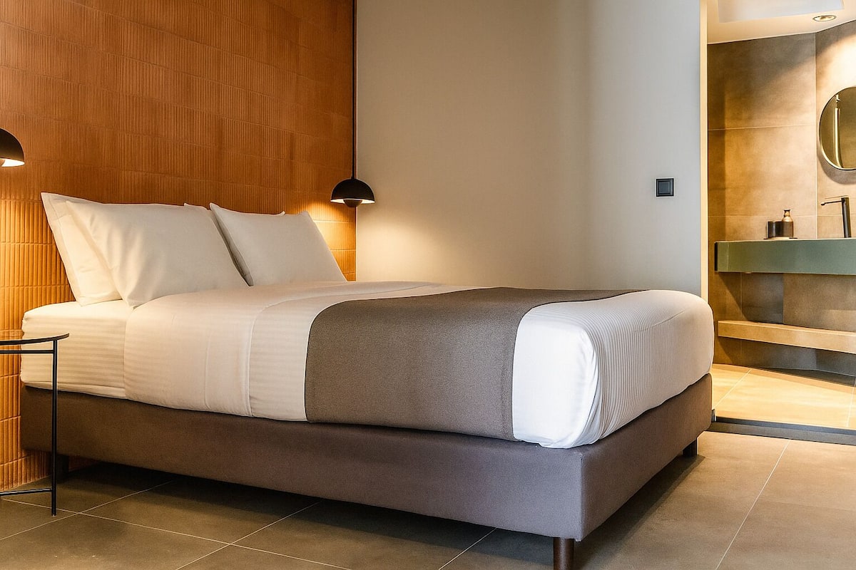 A modern hotel room with a large bed, a bedside table, and a built-in bench.