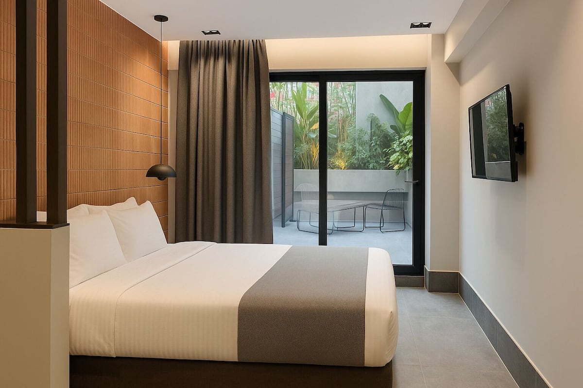 A modern hotel room with a large bed, a sliding glass door to a balcony, and a flat-screen TV mounted on the wall.