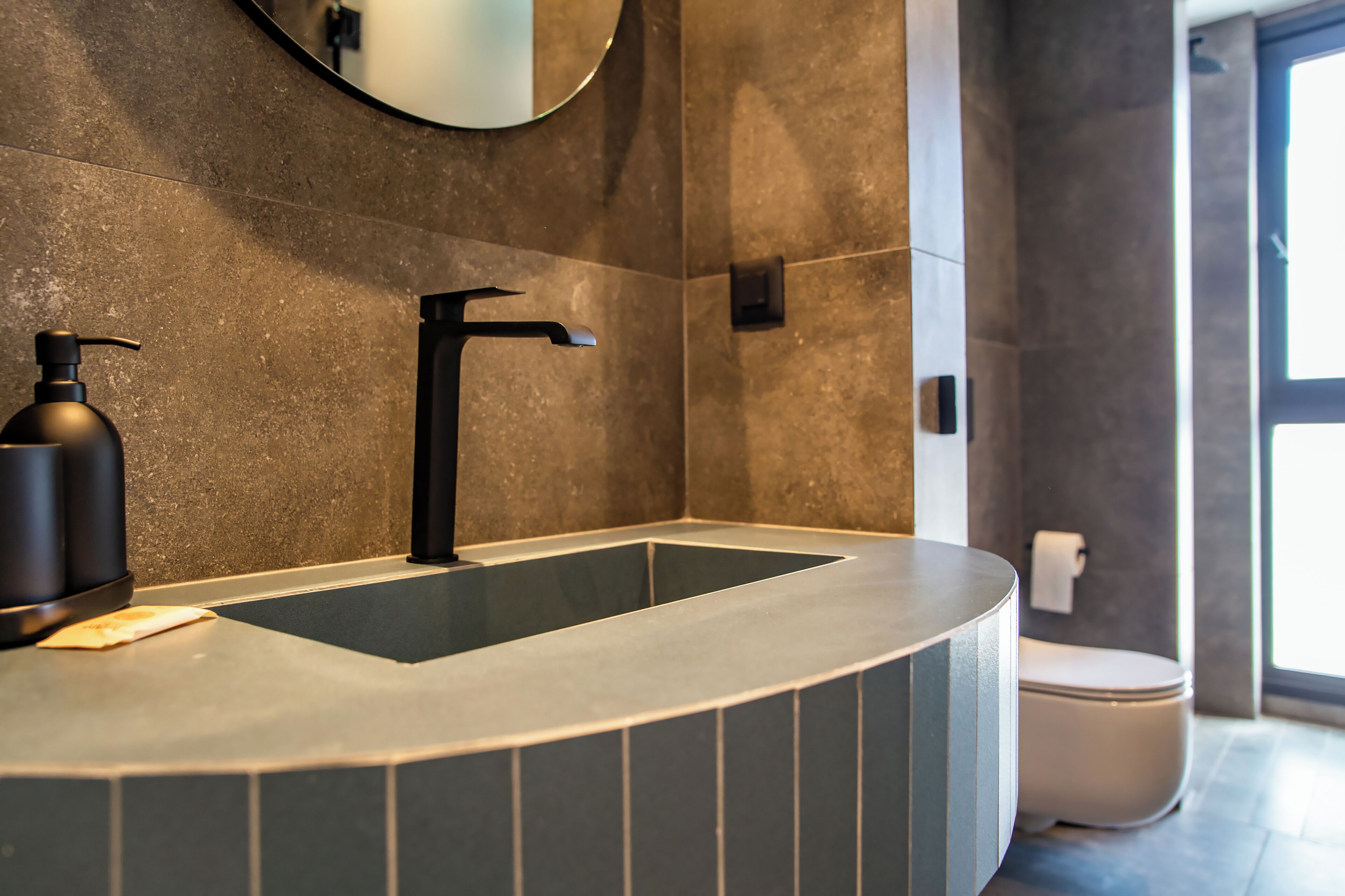 Un bagno moderno con un lavandino curvo, un rubinetto nero e uno specchio grande.