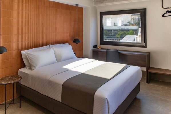 Une chambre d’hôtel moderne, dotée d’un grand lit, d’un bureau et d’une fenêtre donnant sur l’extérieur.