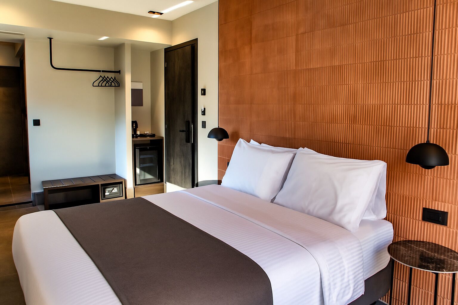 Ein modernes Hotelzimmer mit einem großen Bett, einem Nachttisch, einem Kleiderschrank und einem durch eine offene Tür einsehbaren Badezimmer.
